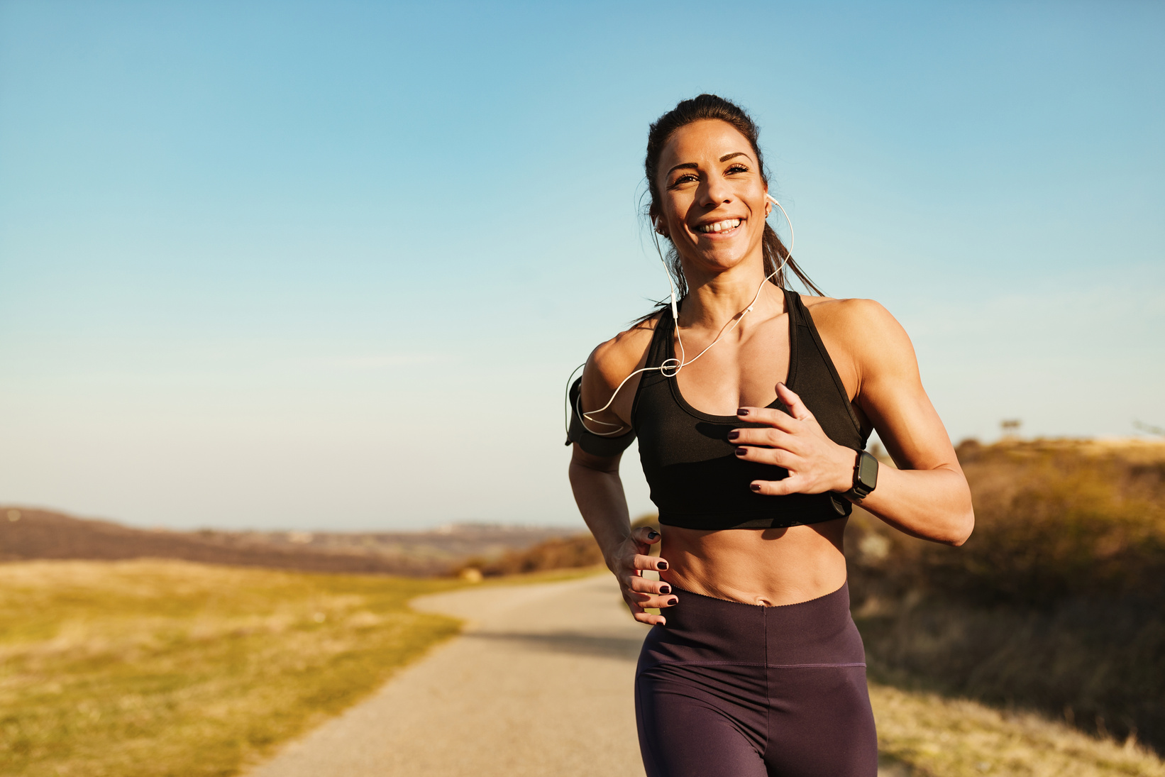 Happy sportswoman running while having sports training in nature.